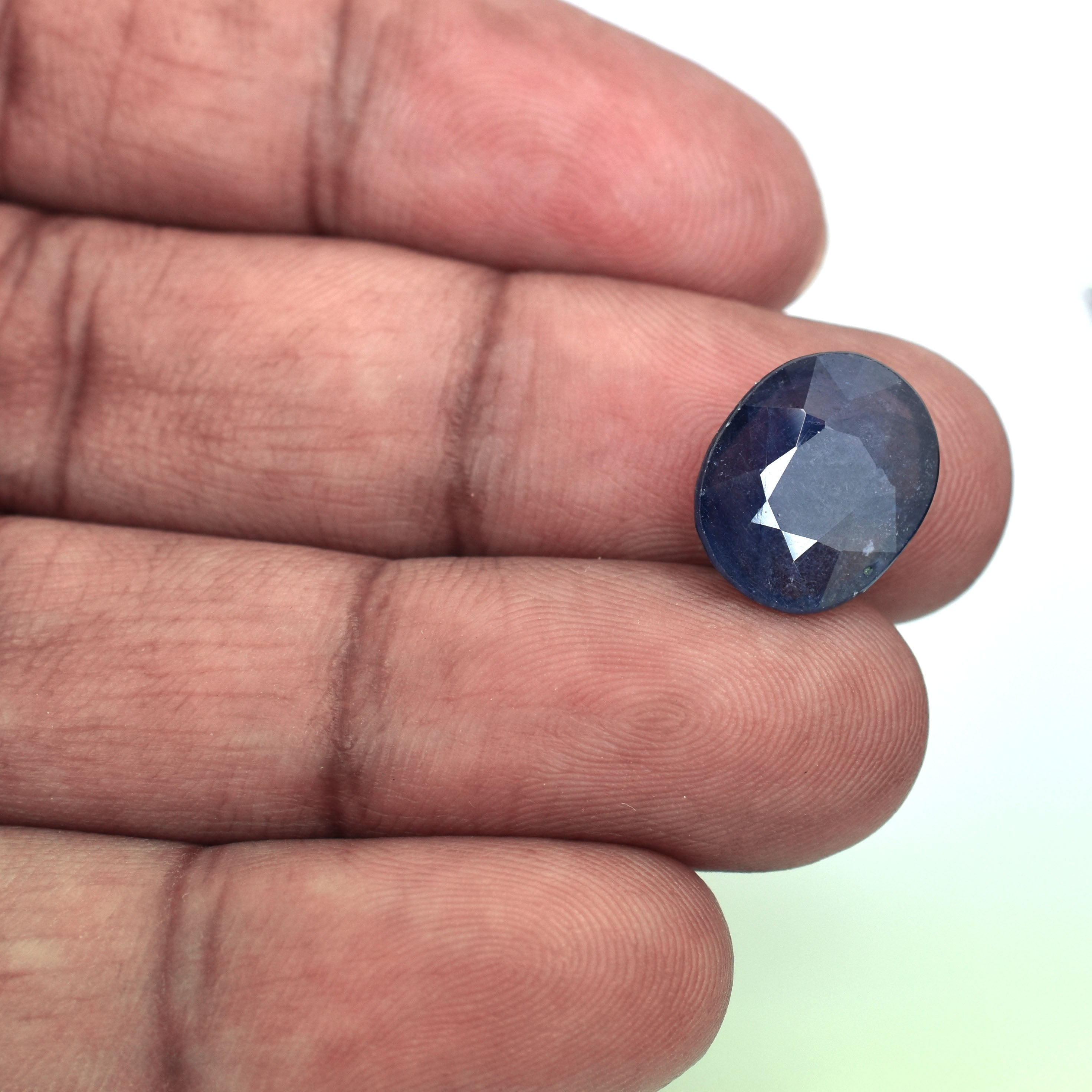 Dark blue oval-cut gemstone held between fingers.