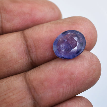 Oval-cut purple gemstone held between two fingers.