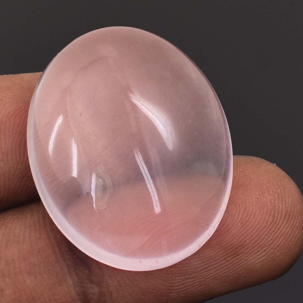 Translucent pink oval gemstone or crystal held between fingers.