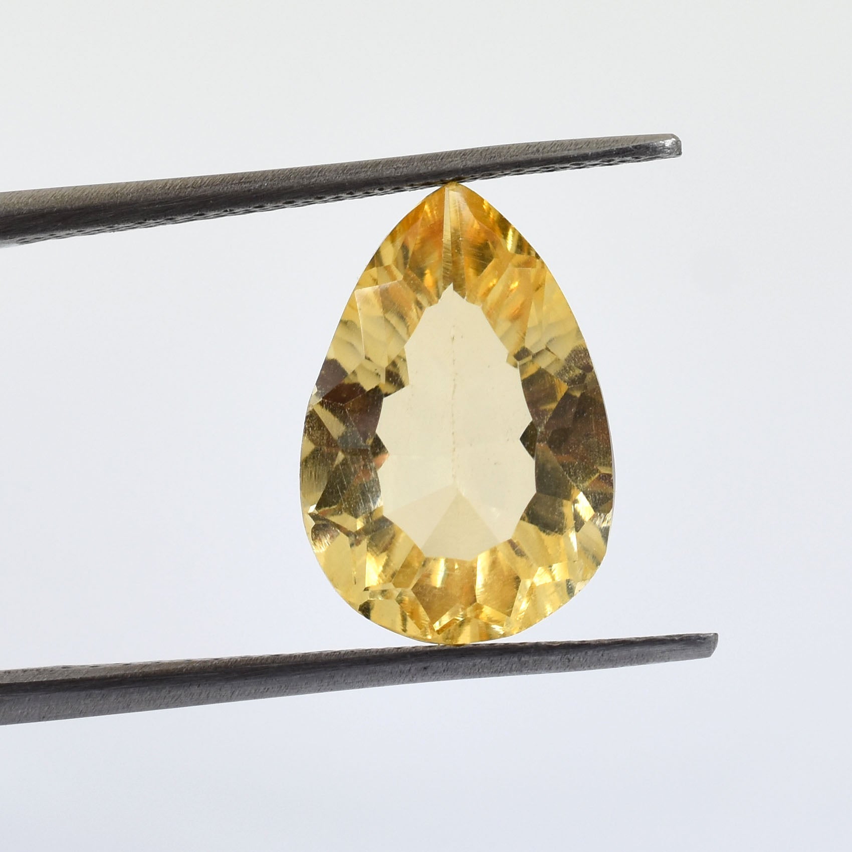 Pear-shaped yellow gemstone held by tweezers.