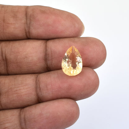 Teardrop-shaped yellow gemstone held between fingers.