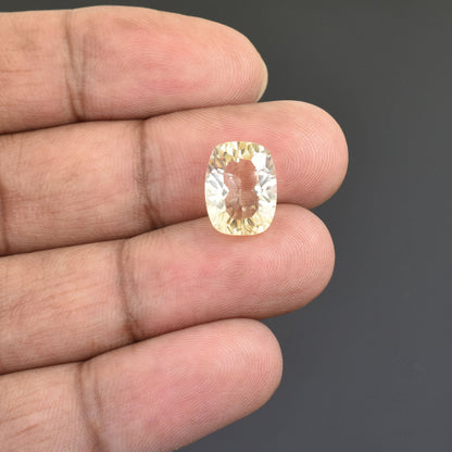 Cushion-cut gemstone with a pale yellow color held between fingers.