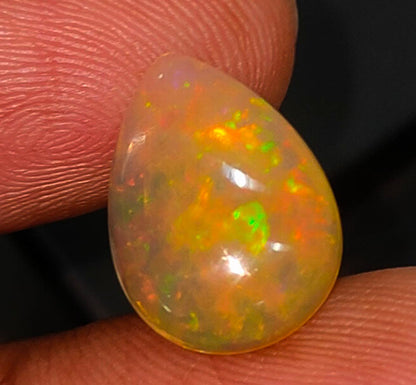 Teardrop-shaped opal gemstone displaying vibrant orange and green fire.