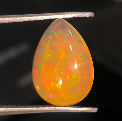 Teardrop-shaped opal gemstone with vibrant orange and yellow fire patterns.