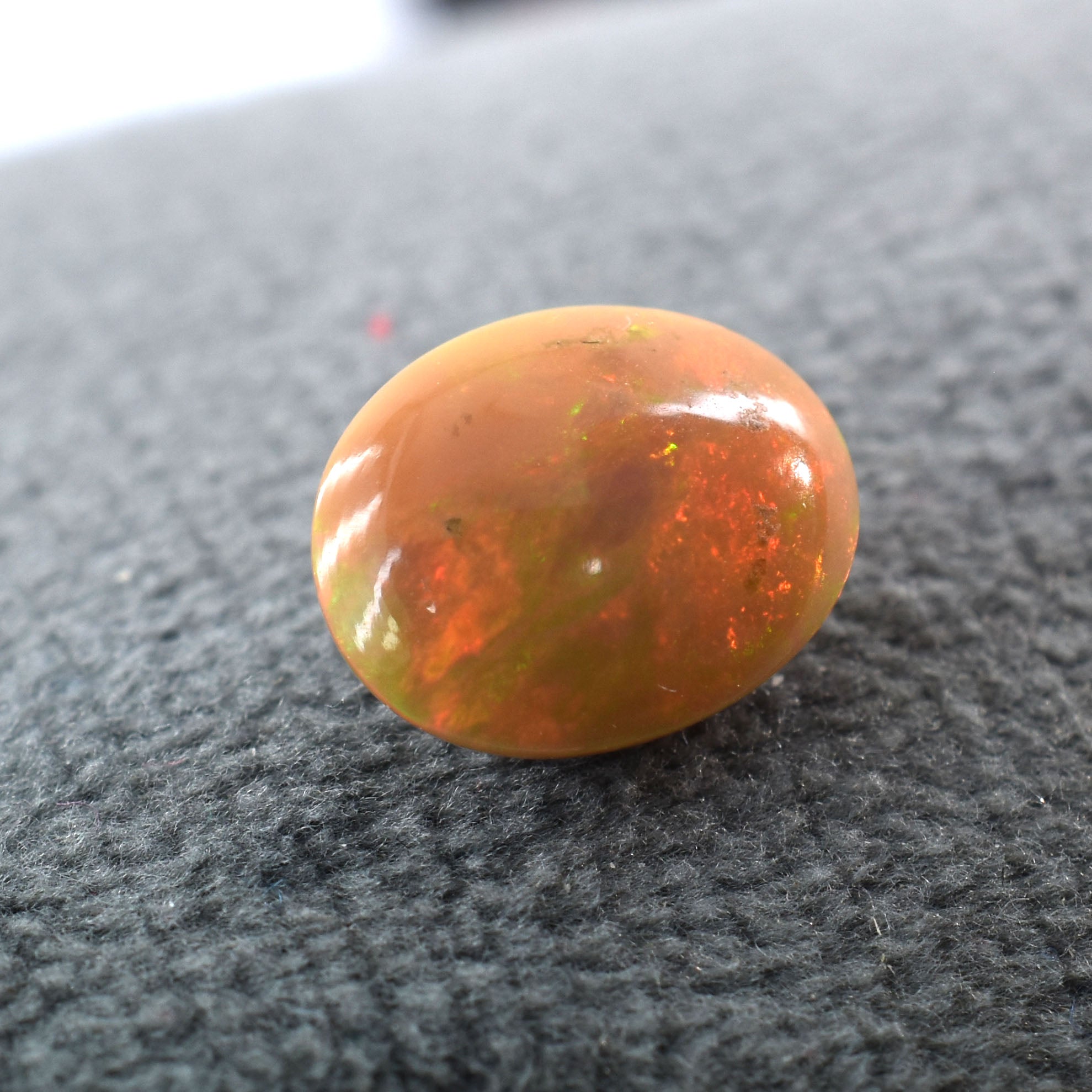 Oval-shaped opal gemstone with orange and red fire patterns.