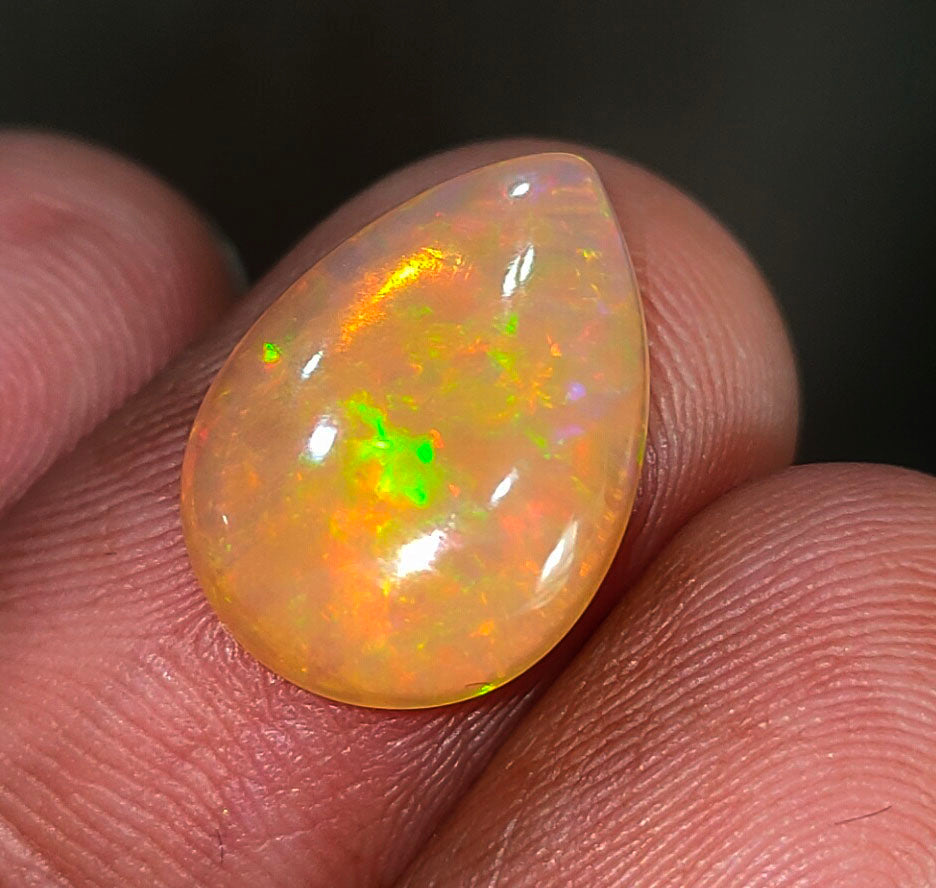 Teardrop-shaped opal gemstone with vibrant green and orange fire patterns.