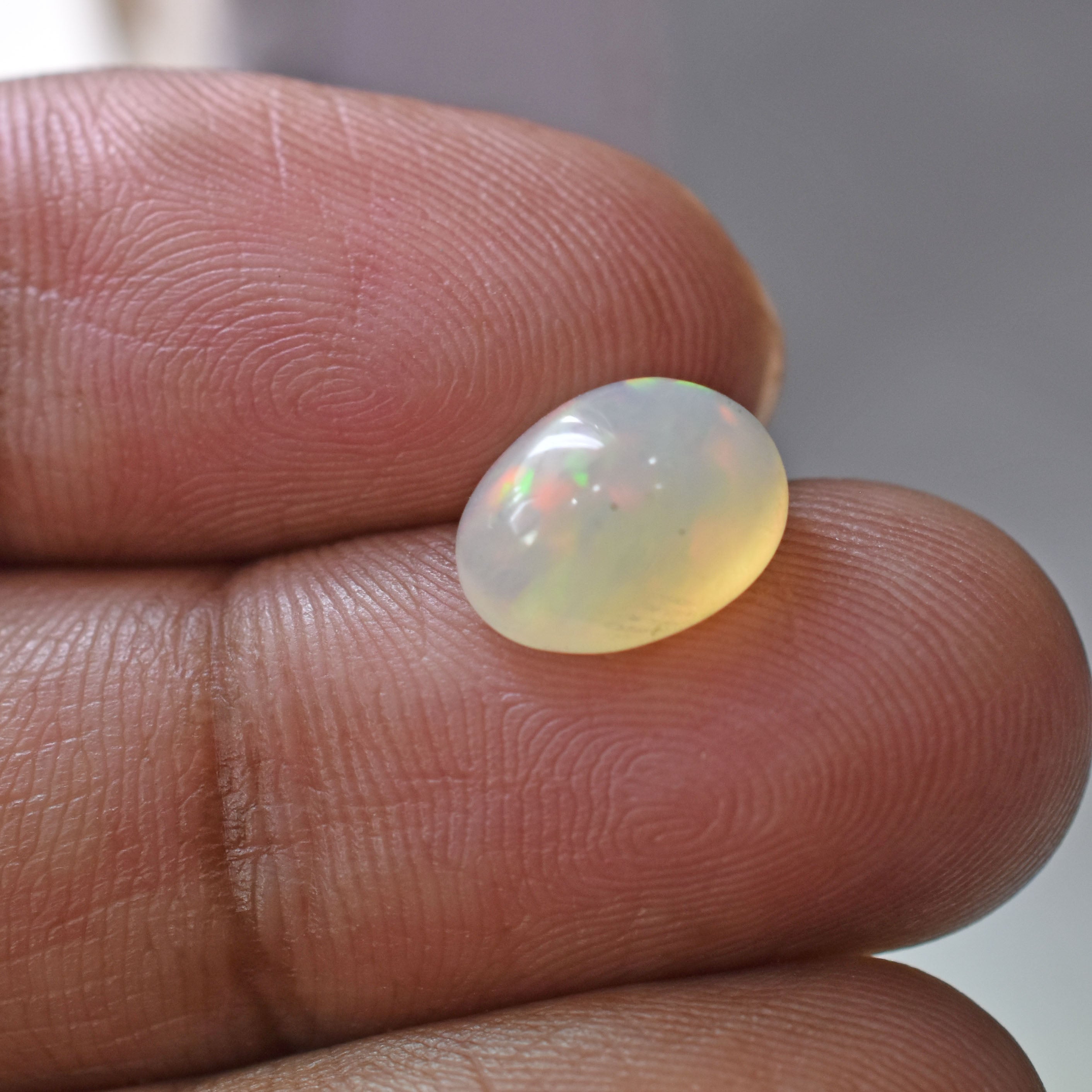 Opal gemstone held between two fingers, displaying a milky white color with subtle iridescent flashes.