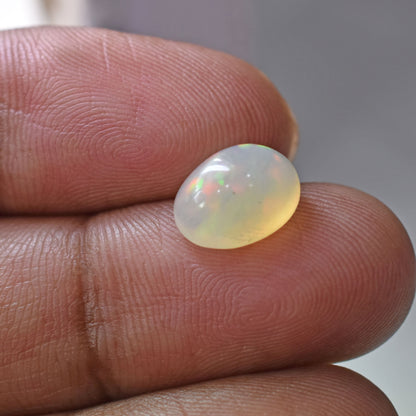 Opal gemstone held between two fingers, displaying a milky white color with subtle iridescent flashes.