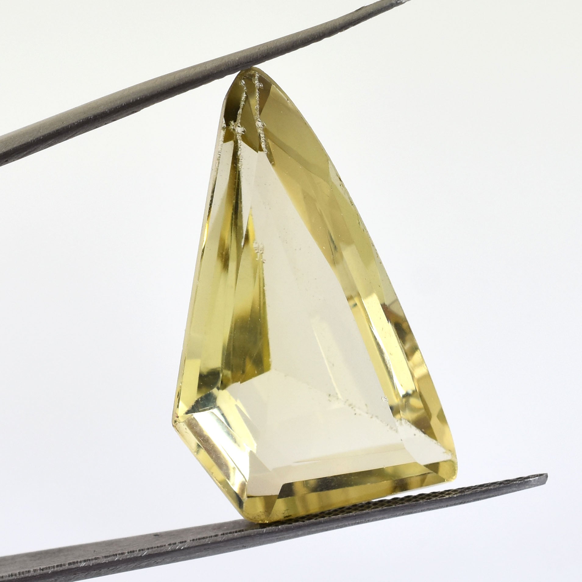 Triangular-cut yellow gemstone held by tweezers.