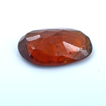 Oval-shaped, reddish-orange gemstone with facets and inclusions.