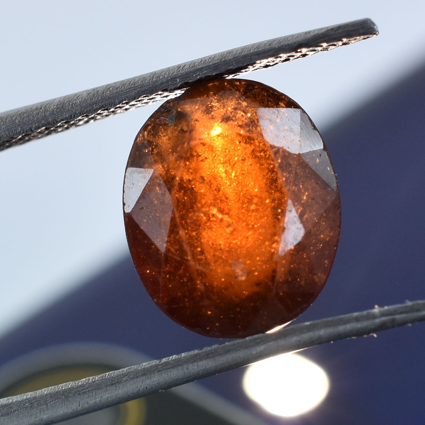 Faceted orange-brown gemstone held by tweezers.