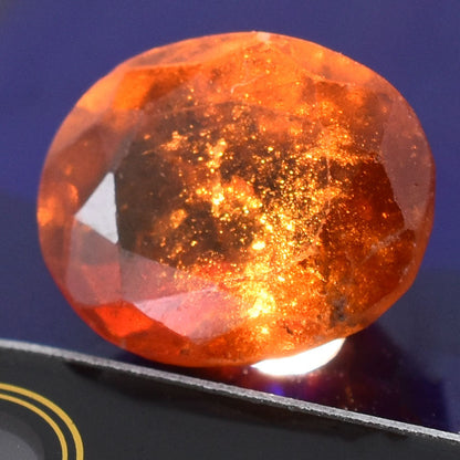 Faceted orange gemstone with internal sparkles and inclusions.