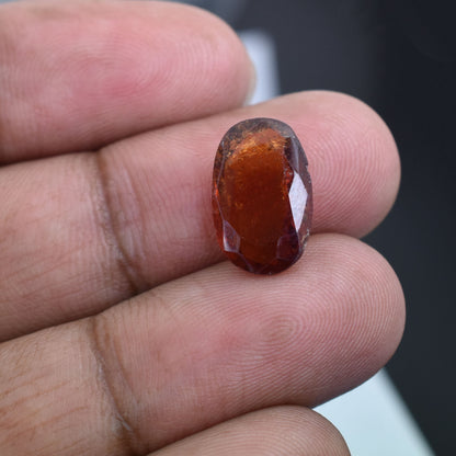 Oval-shaped, reddish-brown gemstone held between fingers.