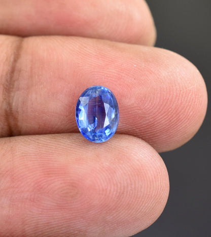 Oval-cut blue gemstone, likely a sapphire, held between fingers.