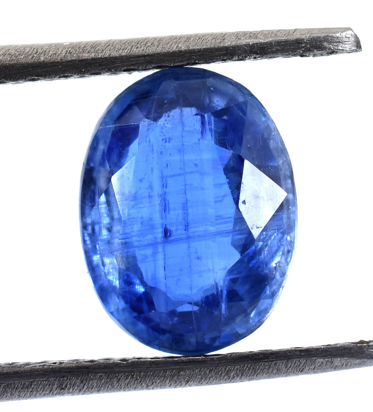 Oval-cut blue gemstone, likely a sapphire, held between metal tweezers or prongs.