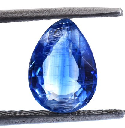 Teardrop-shaped blue gemstone held between tweezers or a jeweler’s tool.