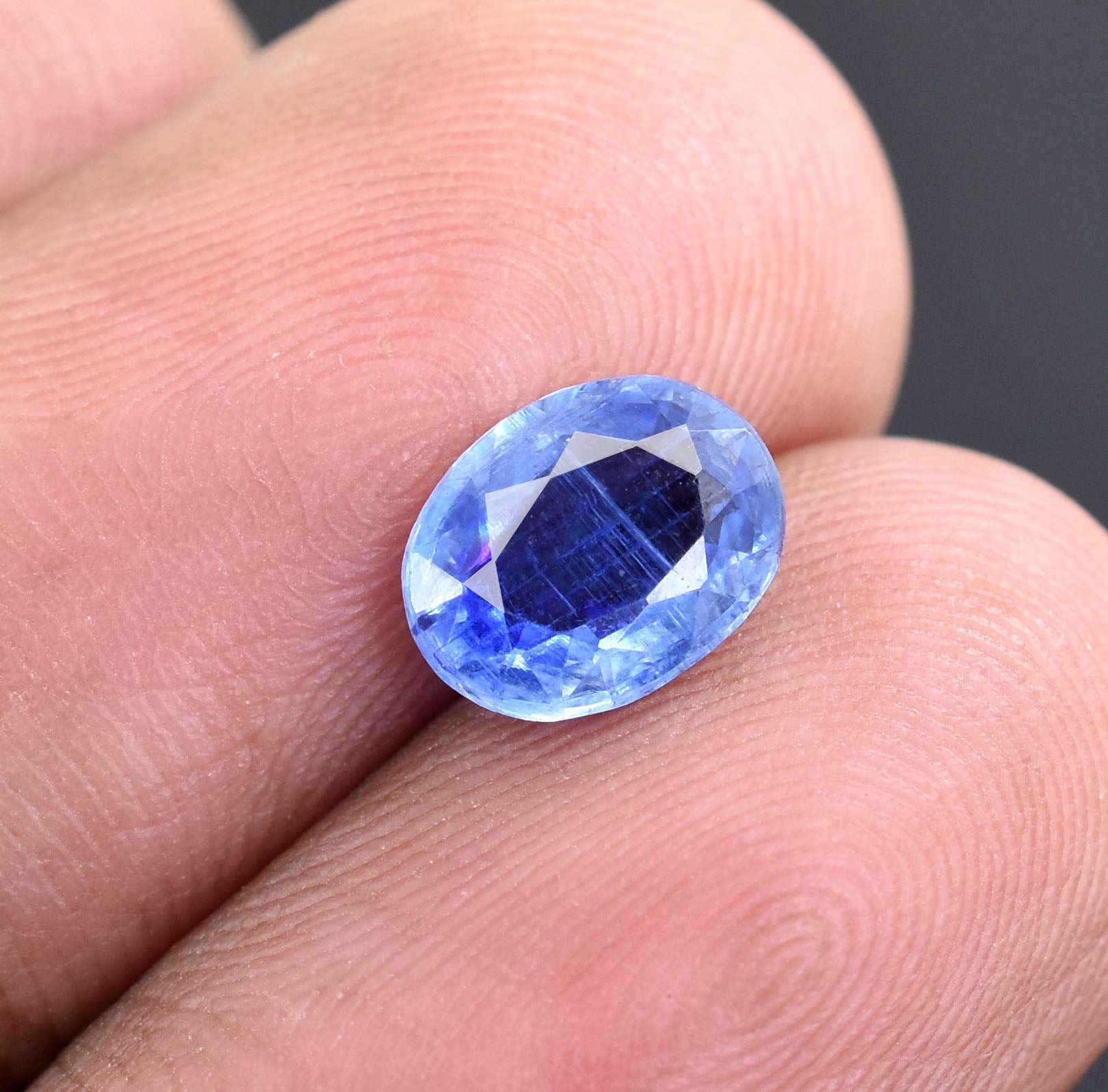 Oval-cut blue sapphire gemstone held between fingers.