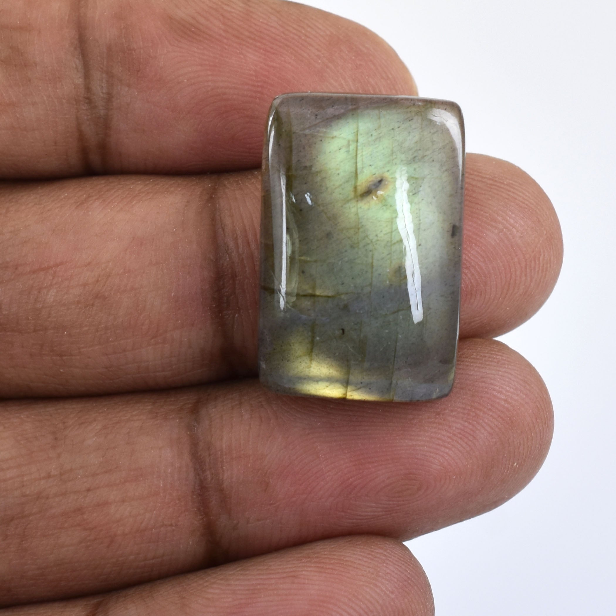 Rectangular gemstone with a cloudy, pale green appearance held between fingers.