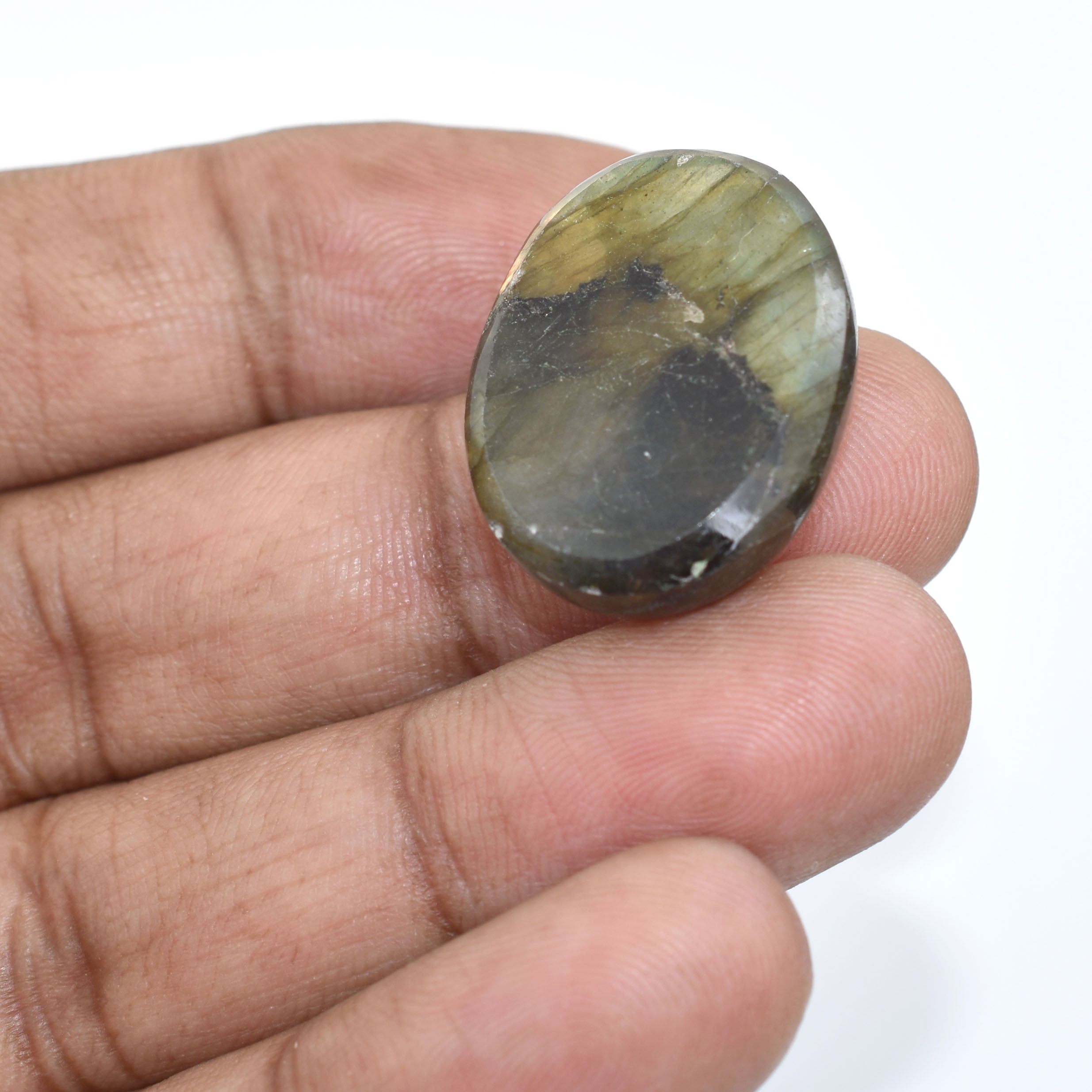 Polished oval gemstone or cabochon with mottled green and gray coloration held between fingers.