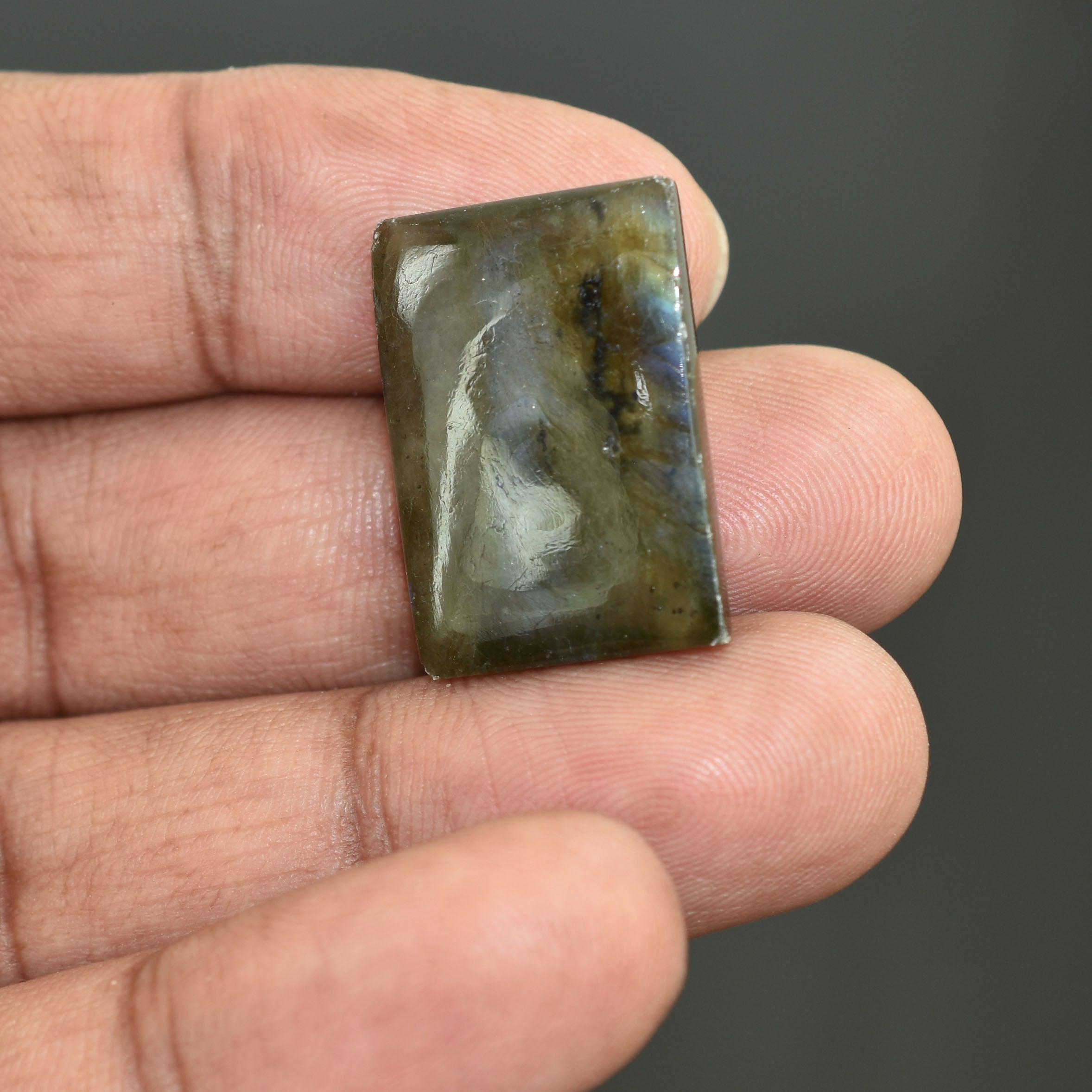 Rectangular gemstone or polished stone with swirling patterns held between fingers.