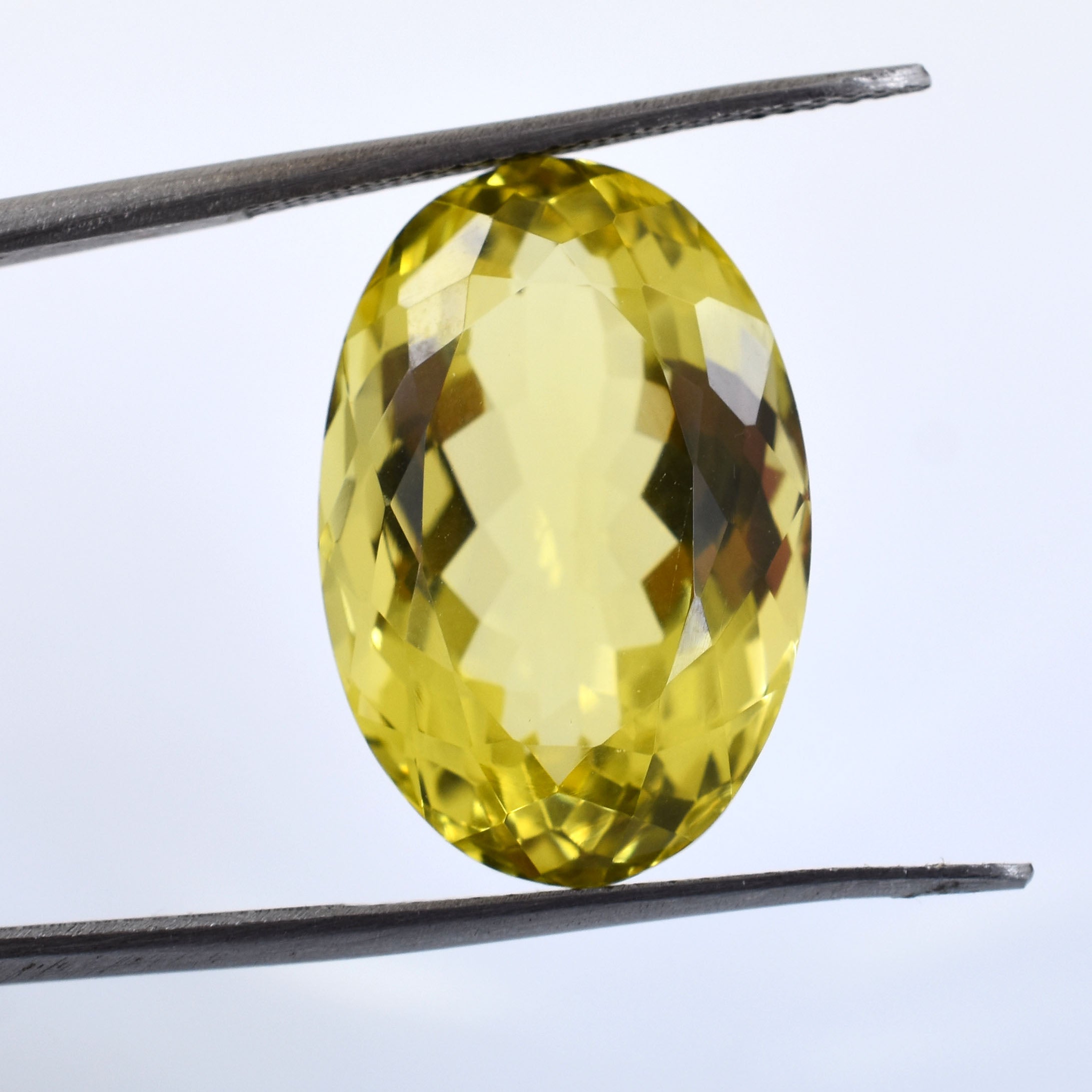 Oval-cut yellow gemstone held between tweezers.