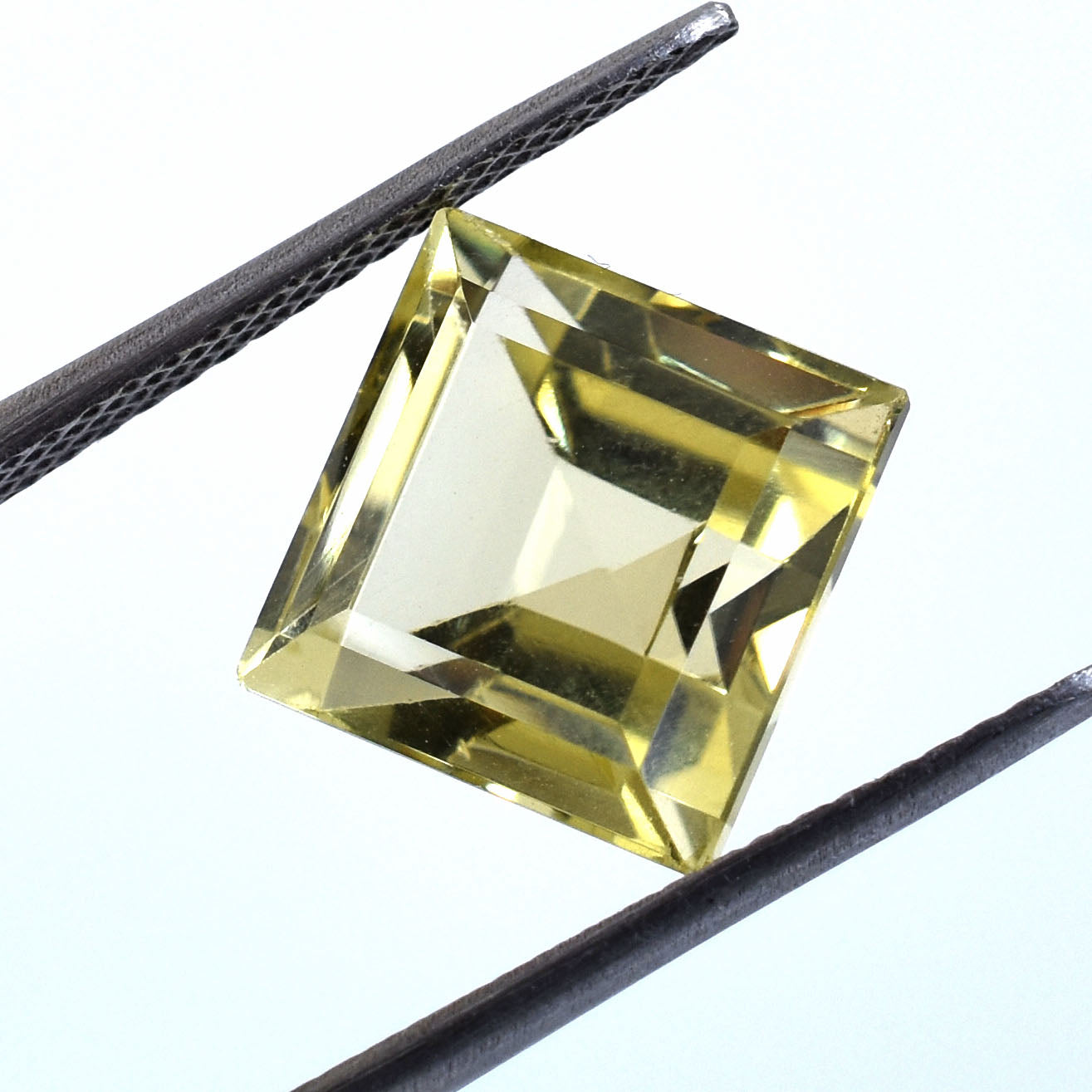 Square-cut yellow gemstone held between tweezers.