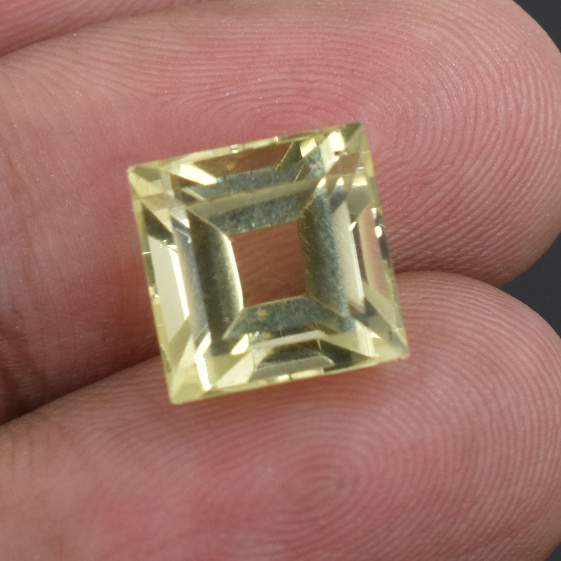 Square-cut yellow gemstone held between fingertips.