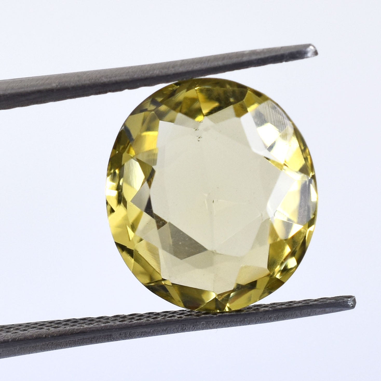 Faceted yellow gemstone held by tweezers.