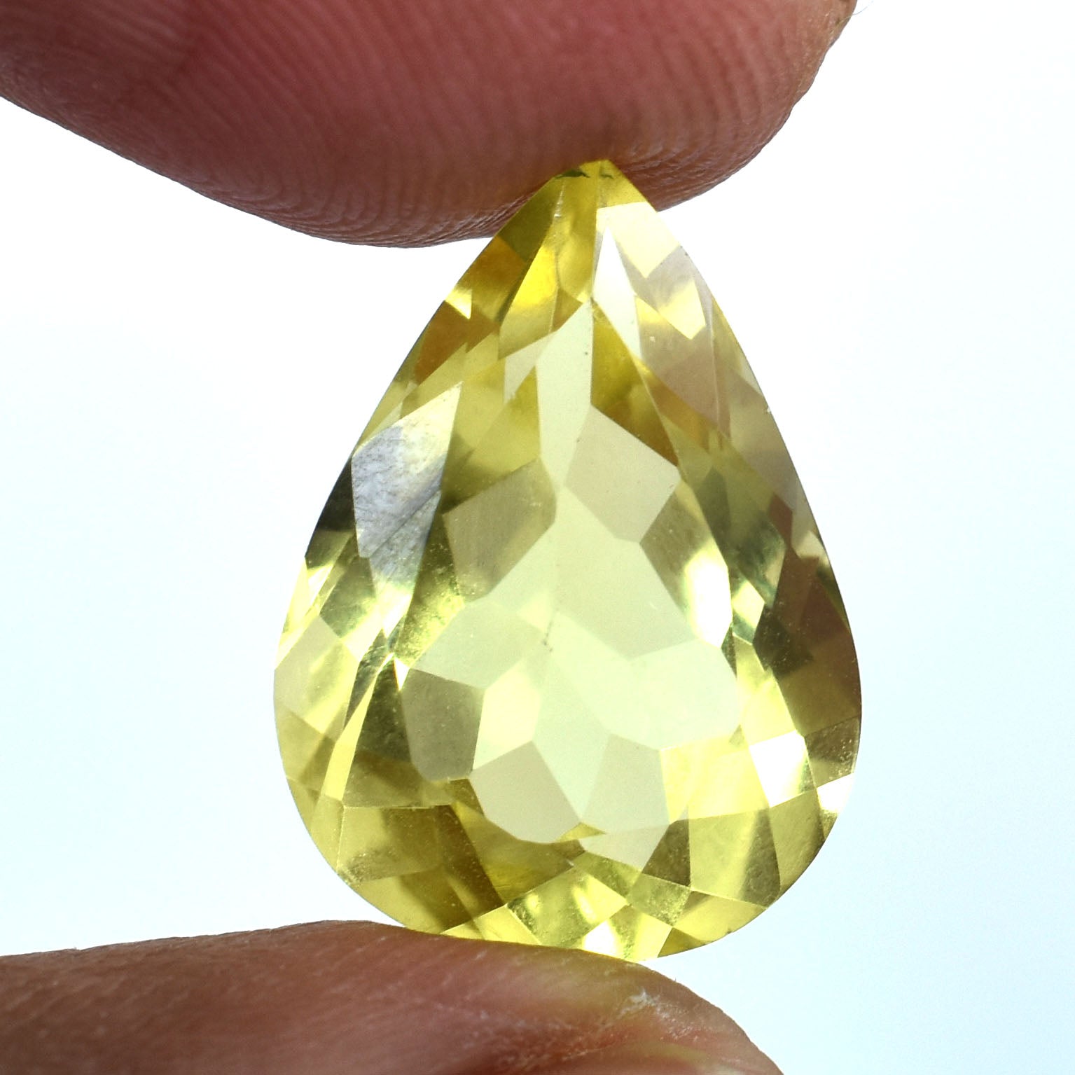 Teardrop-shaped yellow gemstone held between fingers.