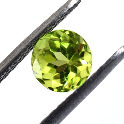 Round-cut peridot gemstone held between tweezers.