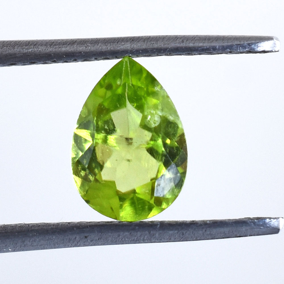 Pear-shaped, bright green gemstone held between tweezers.