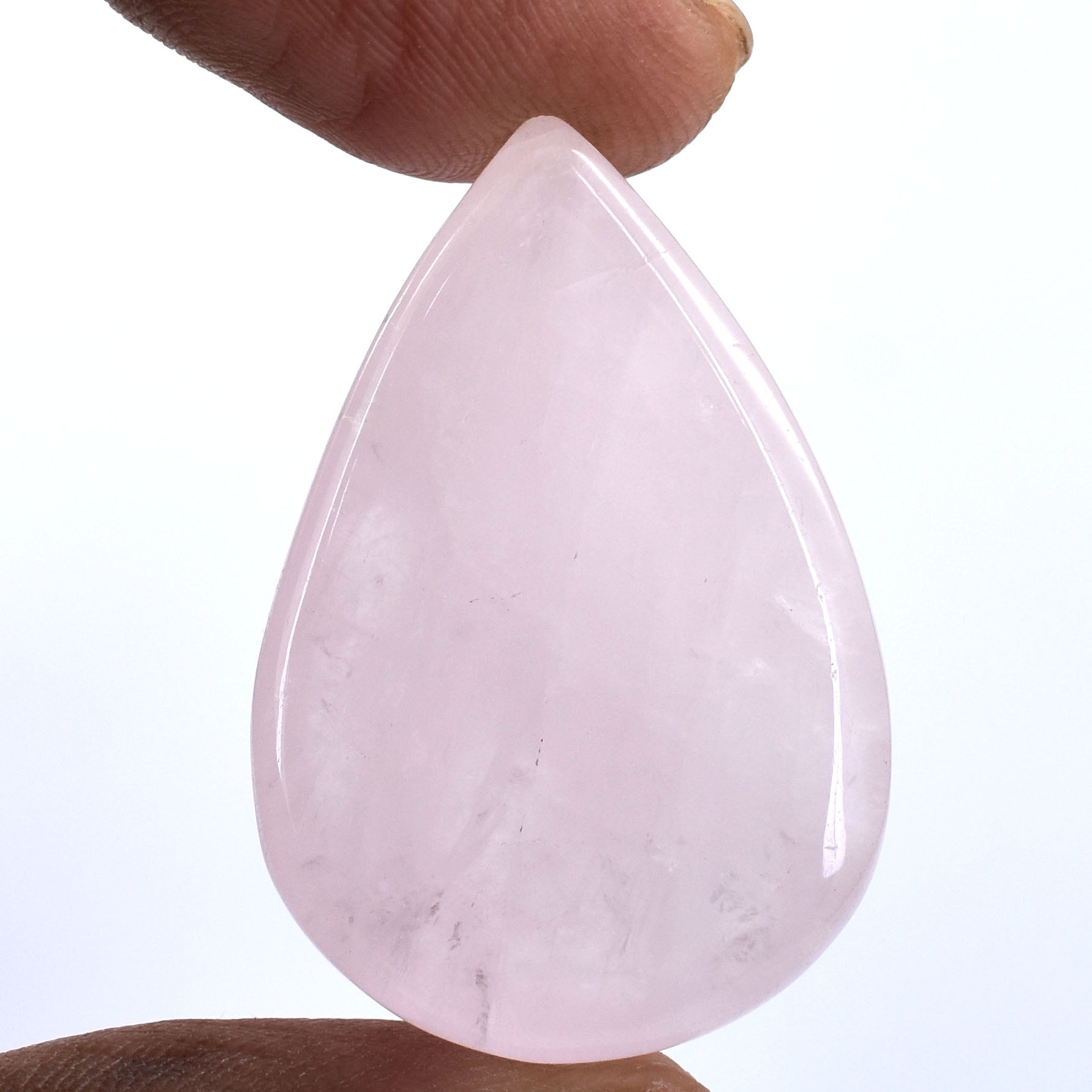 Teardrop-shaped pale pink gemstone or crystal held between fingers.