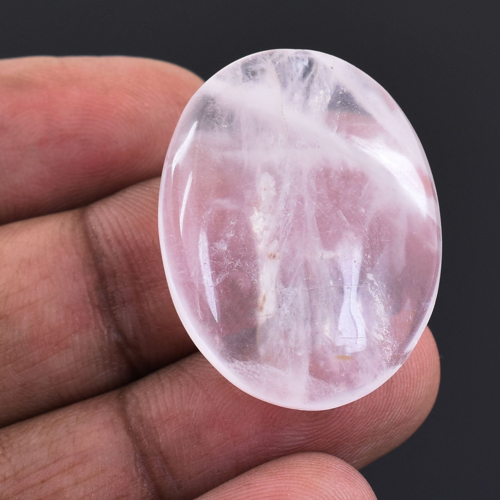 Oval-shaped, translucent pink crystal or gemstone held between fingers.