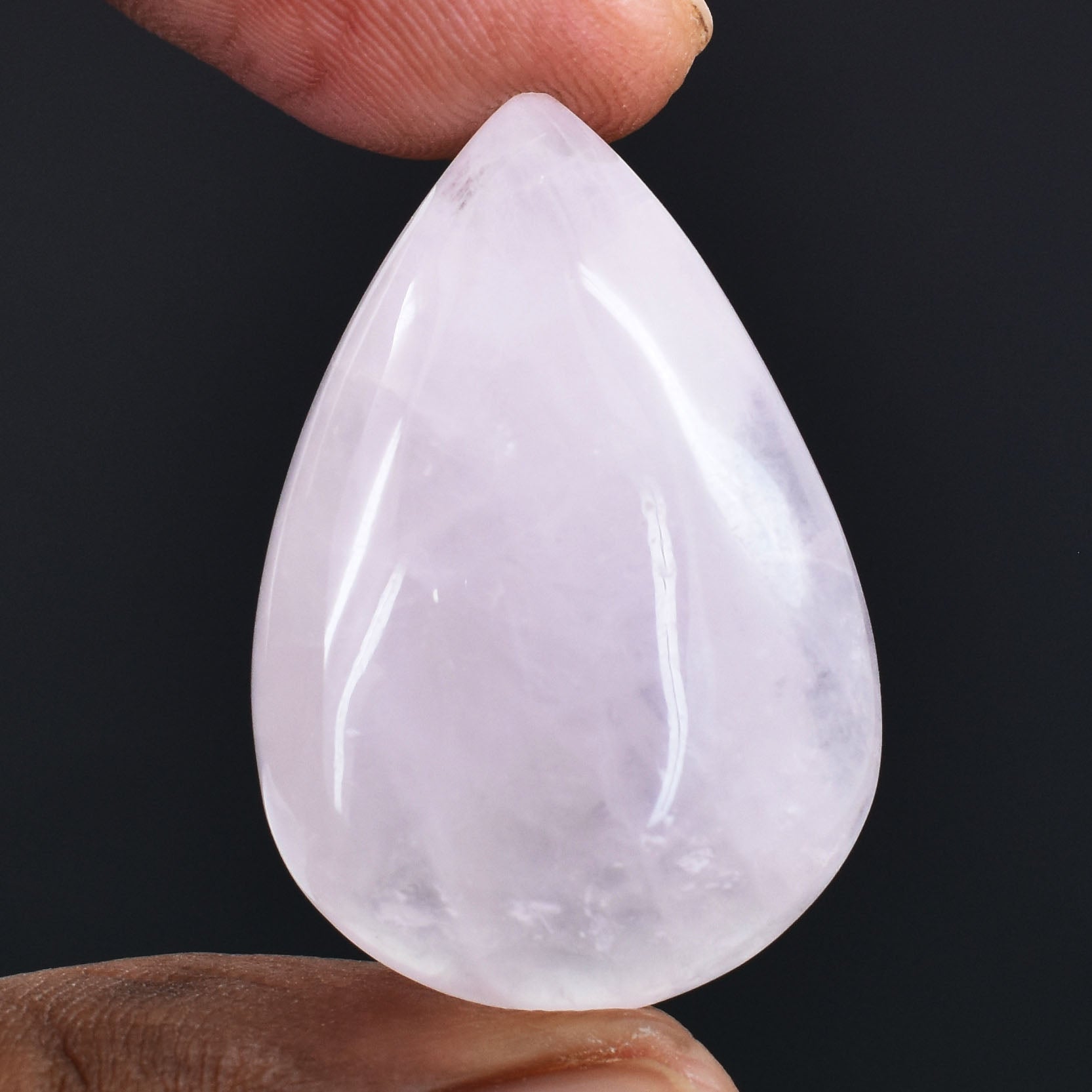 Teardrop-shaped white gemstone or crystal held between two fingers.