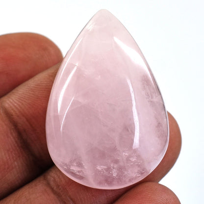 Teardrop-shaped rose quartz crystal held between fingers.