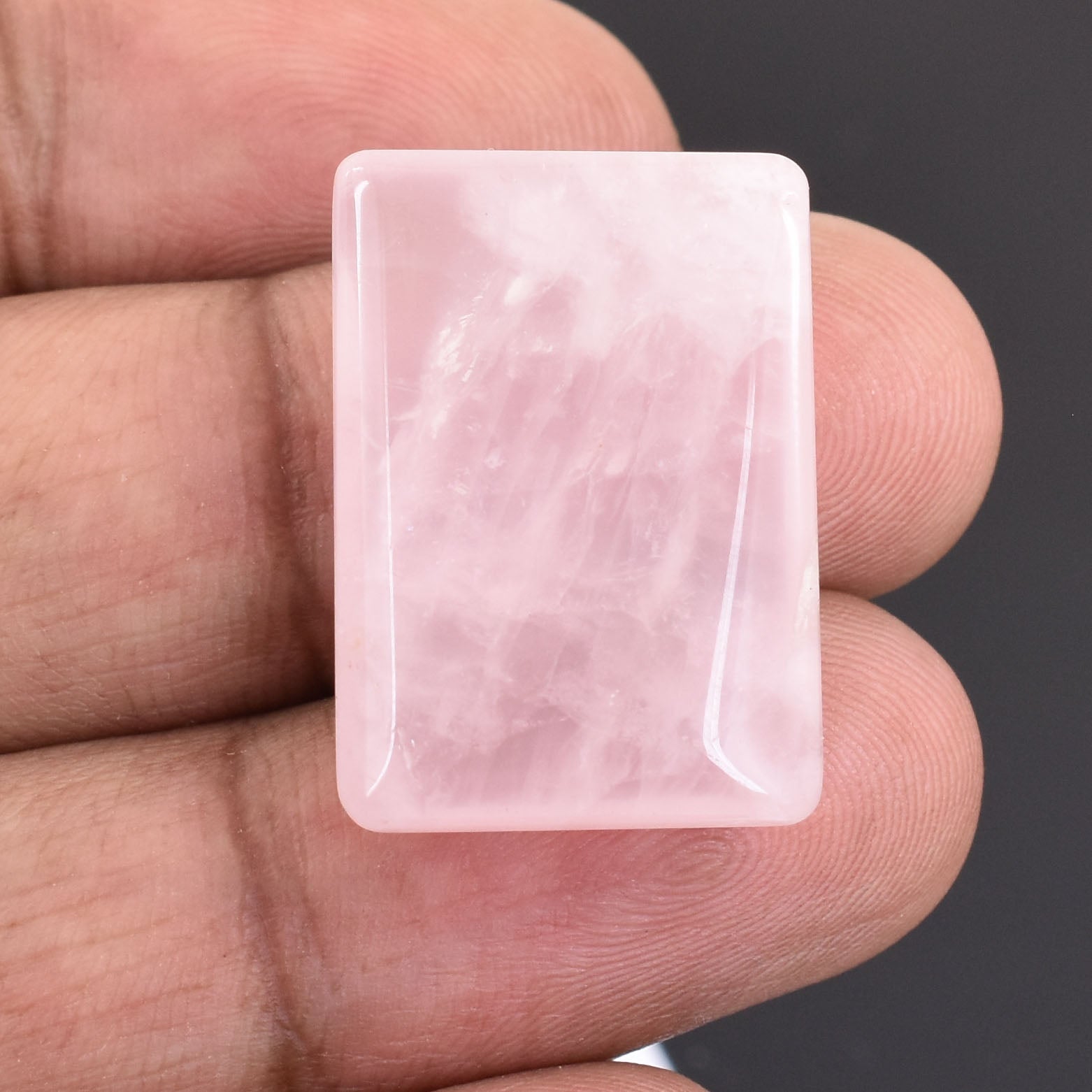 Rectangular, translucent pink patch or pad held between fingers.