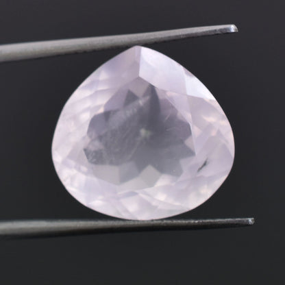 Pear-shaped, translucent gemstone held between tweezers.