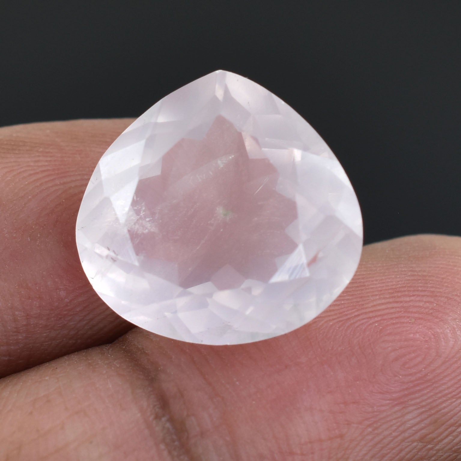 Teardrop-shaped pale pink gemstone held between fingers.