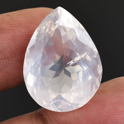 Teardrop-shaped, faceted clear gemstone held between two fingers.