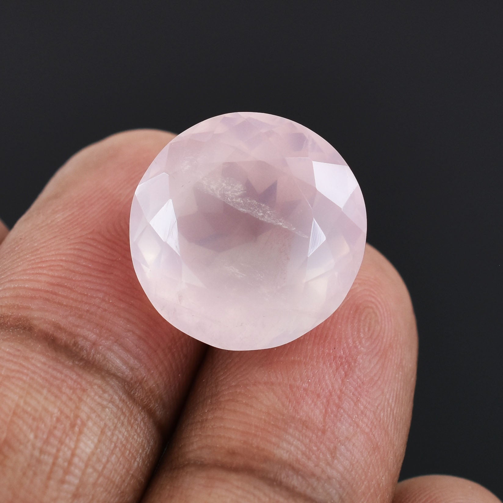 Round, pale pink gemstone or crystal held between fingertips.