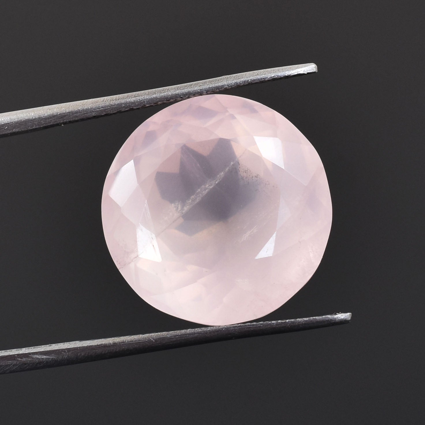 Pink gemstone or crystal held by tweezers, with a dark inclusion visible inside.