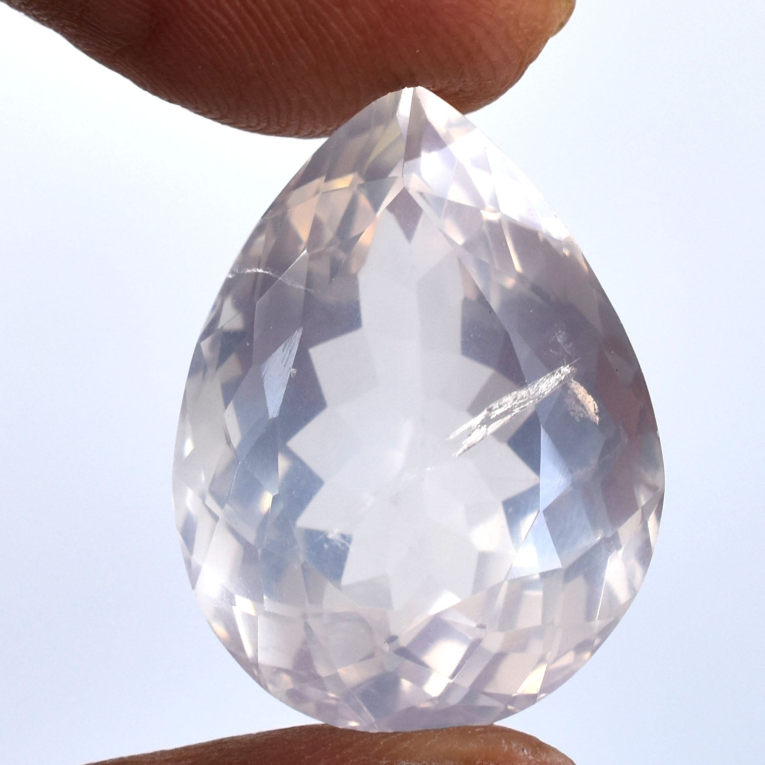 Teardrop-shaped, faceted clear gemstone held between fingers.