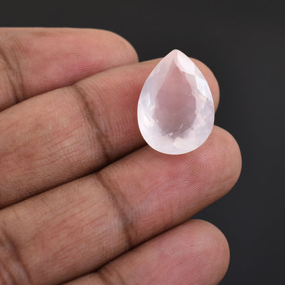 Teardrop-shaped, translucent pink gemstone held between fingers.