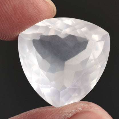 Triangular-cut, faceted clear gemstone held between two fingers.