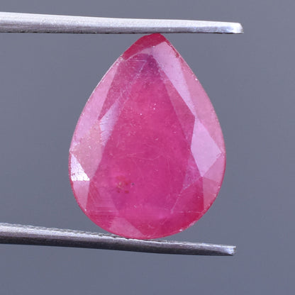 Pear-shaped pink gemstone, likely a ruby or pink sapphire, held by tweezers.