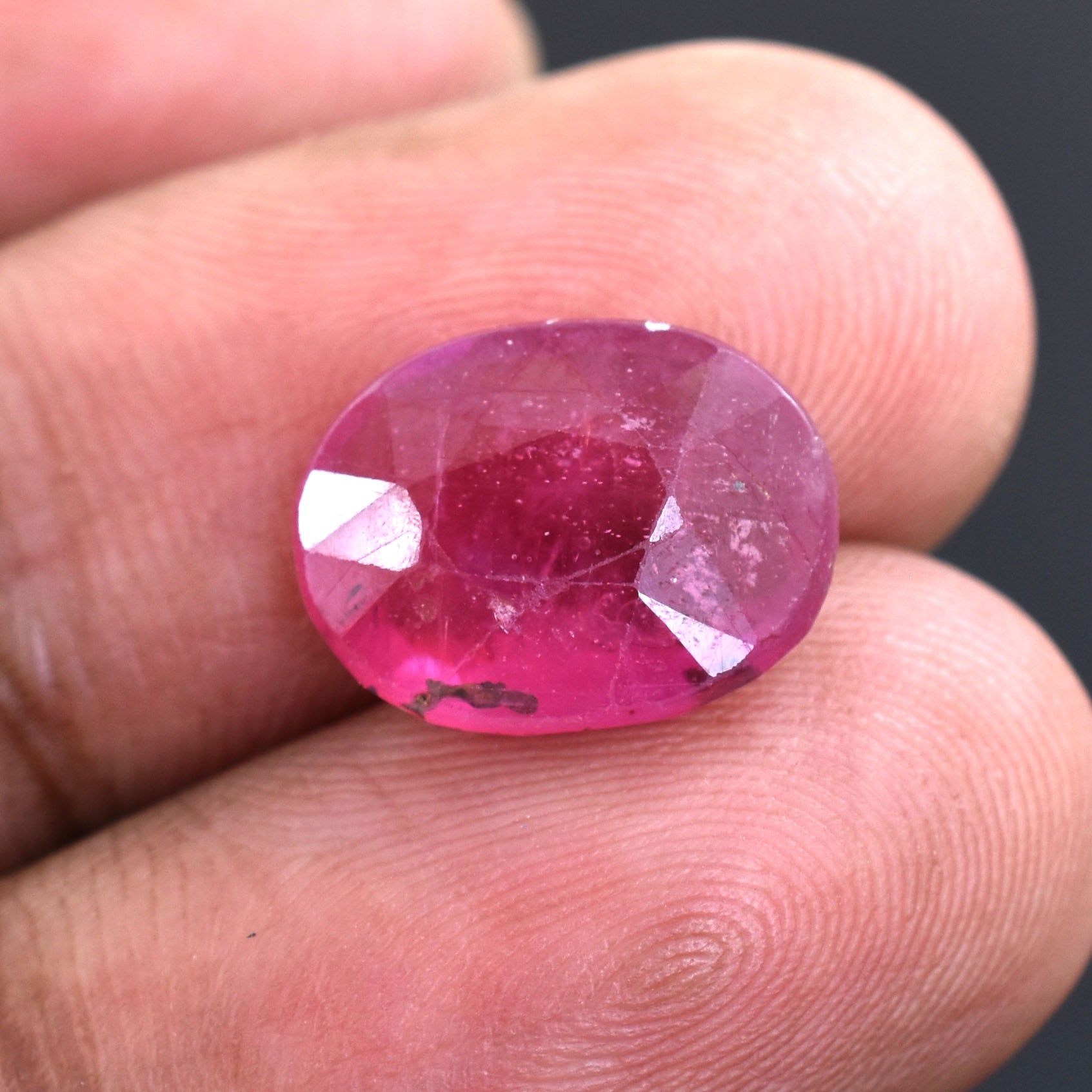 Oval-cut pink gemstone held between fingertips.