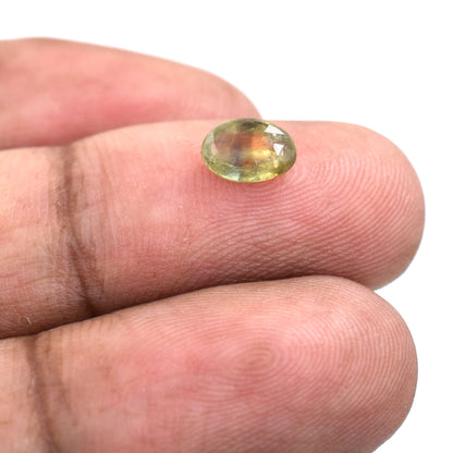 Oval-cut gemstone with yellow-green coloration held on a fingertip.