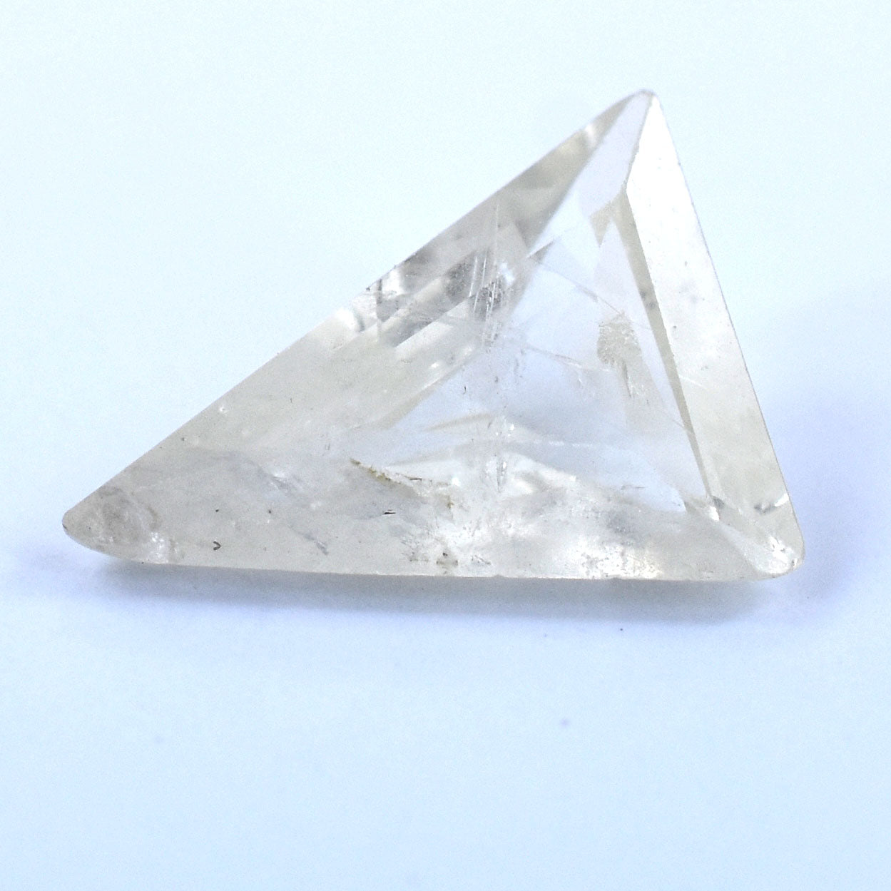 Triangular clear crystal or gemstone with faceted surfaces.