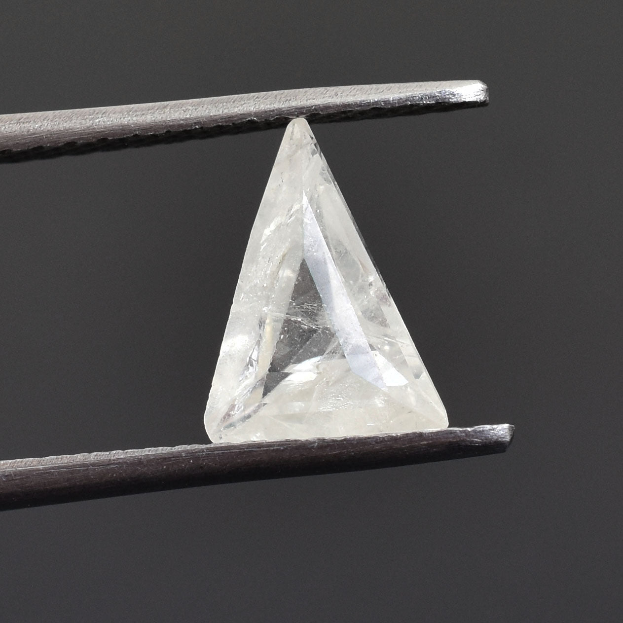 Triangular, transparent gemstone or crystal held between tweezers.