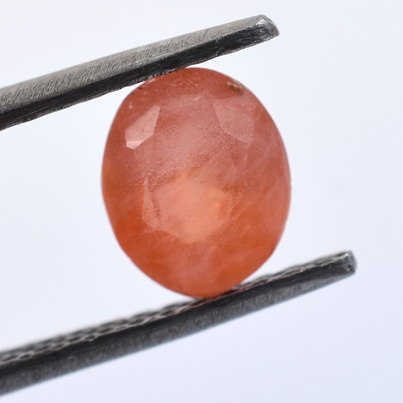 Oval-shaped, translucent orange gemstone held between tweezers.